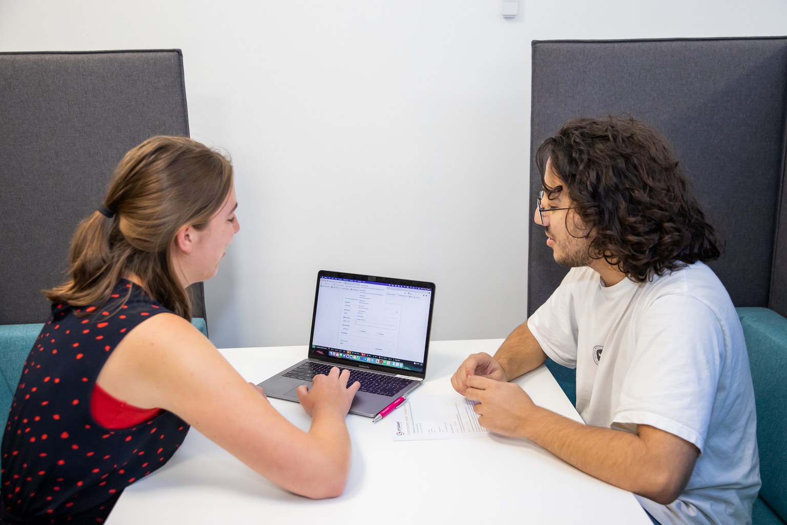Een studente en haar coach werken samen aan een laptop, elk aan een kant van de tafel