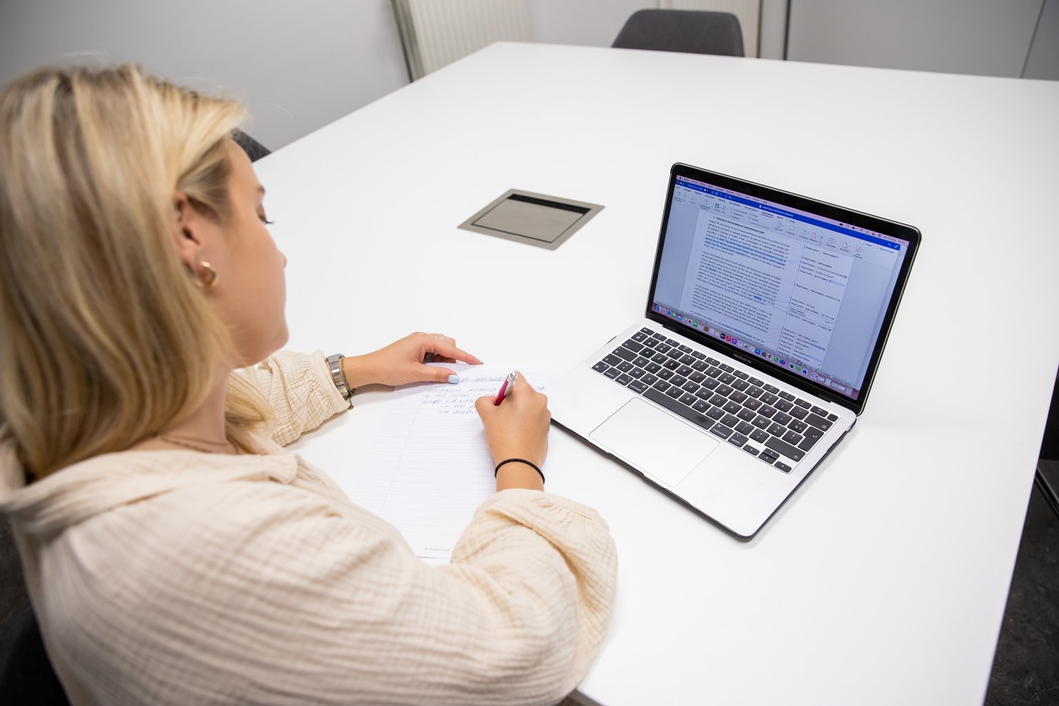 Een studente maakt notities naast haar laptop tijdens het studeren